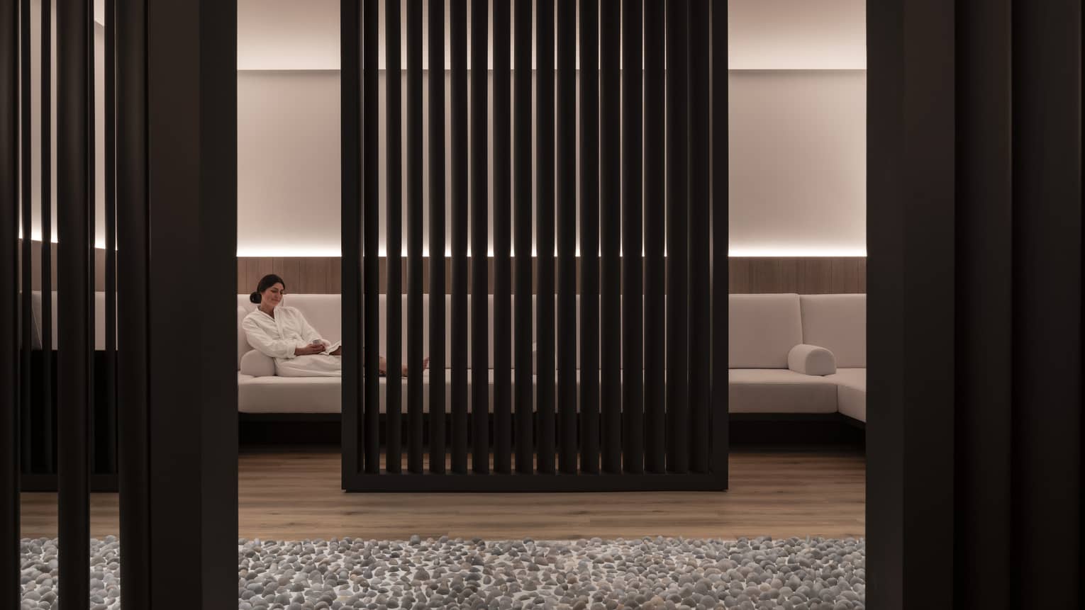 A woman lounges on a large white couch obscured by a black privacy wall. 