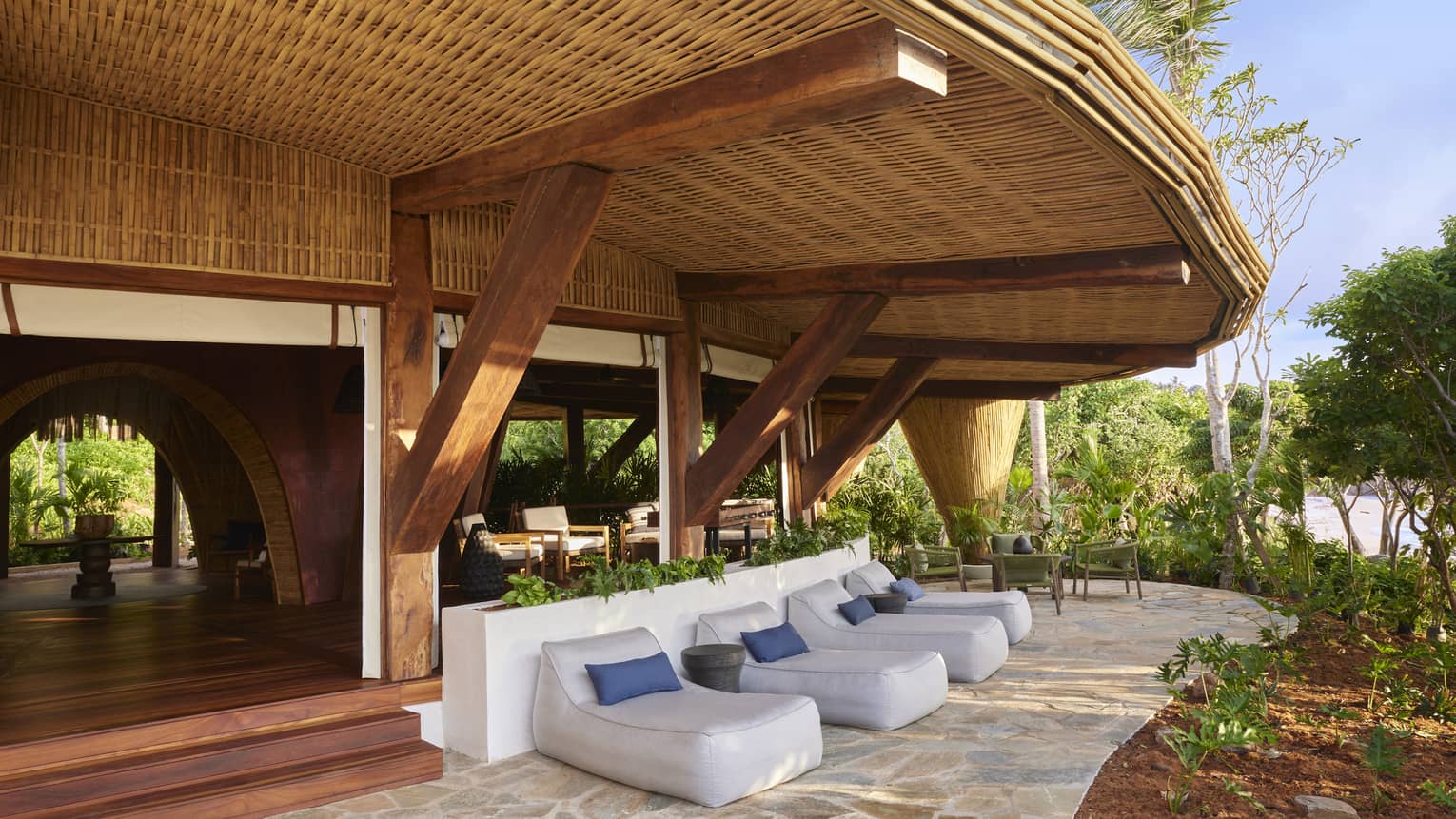 Natural wood-covered restaurant terrace and lounge chairs, surrounded by lush jungle