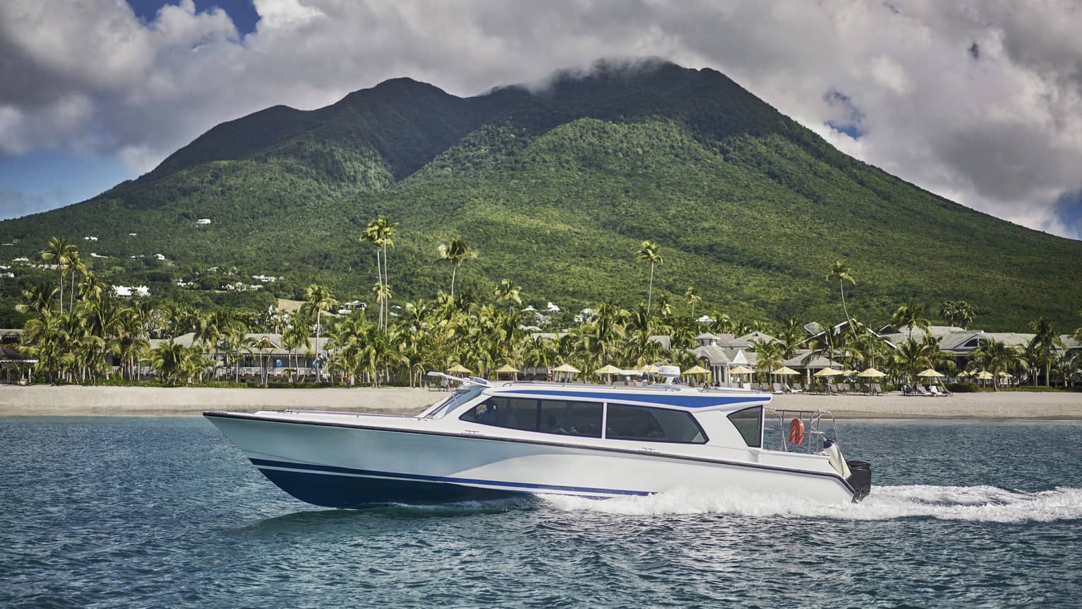 A boat moving across the water with a beach and mountain in the distance.