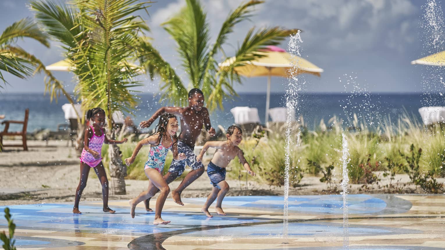 Four children running through a fountain park.