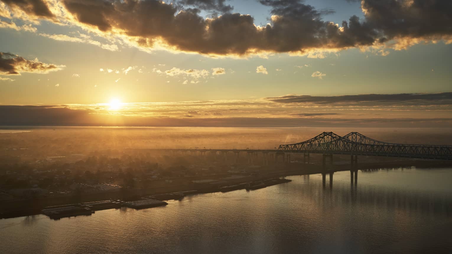 A sunrise near New Orleans bridge crossing a river.