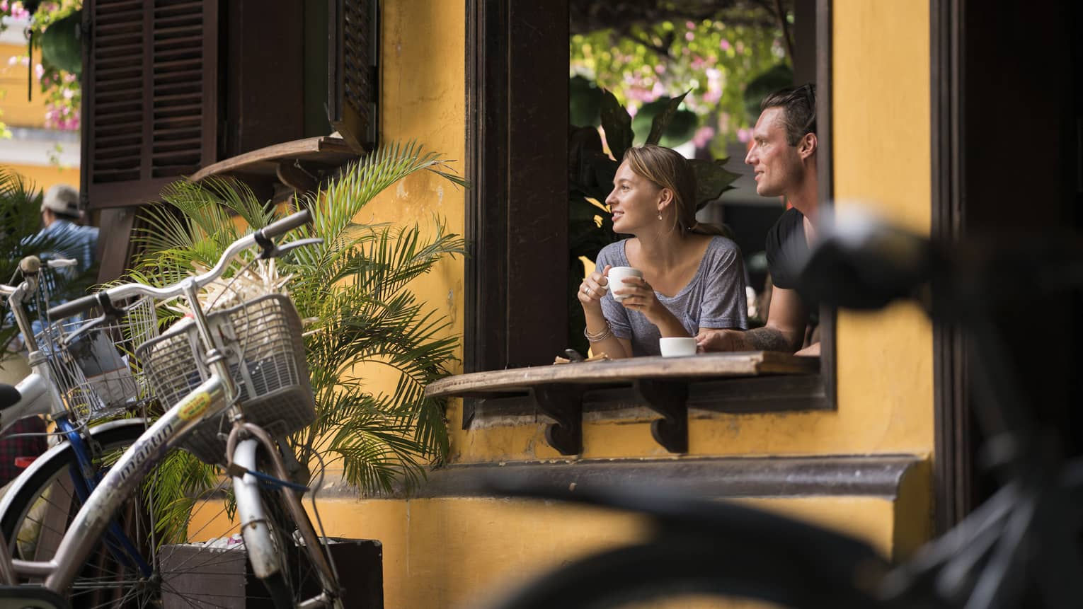 A woman and man looking through a window of a yellow cafe in Hoi, Viet Nam