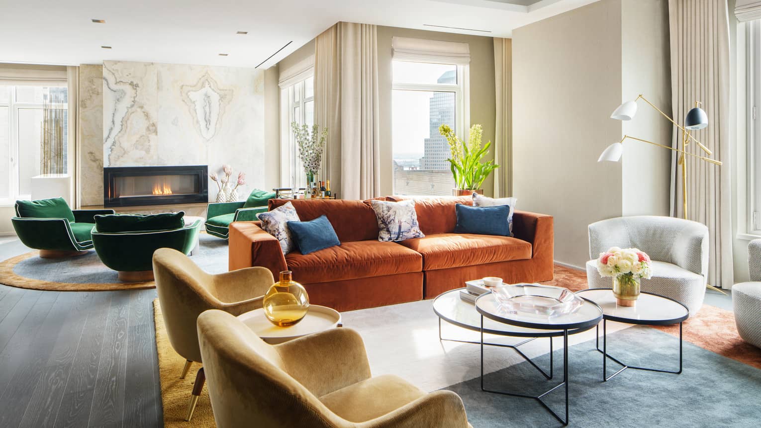 Living area with two mustard-coloured velvet chairs, orange velvet sofa, plus a fireplace area with green arm chairs