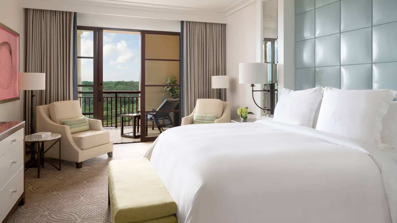 Hotel room with white king bed, light blue head board, beige armchair, walk-out balcony
