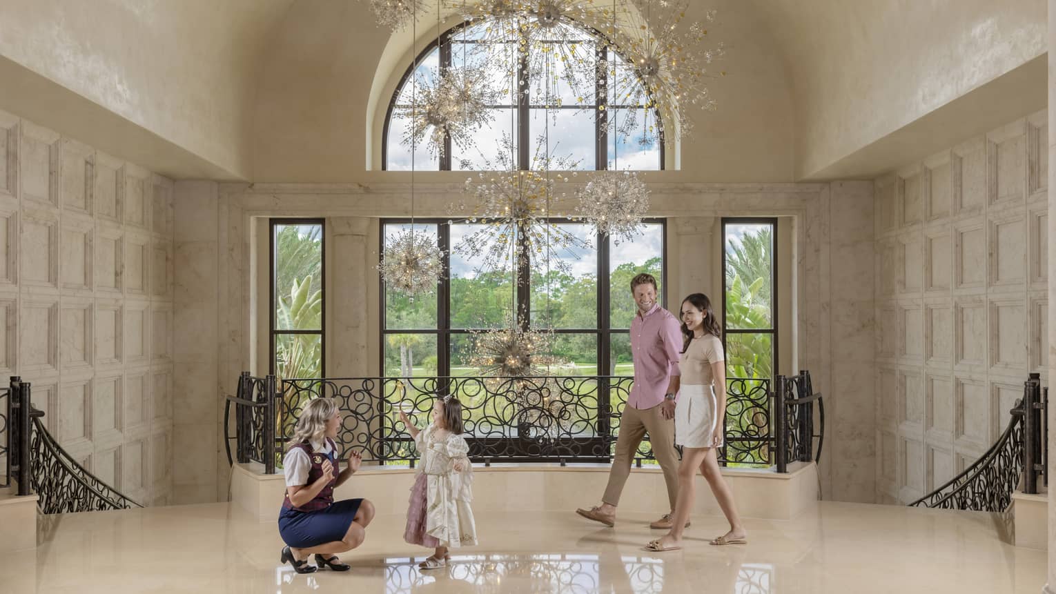 A man and woman walking behind a small child talking to a staff member in a large entryway.