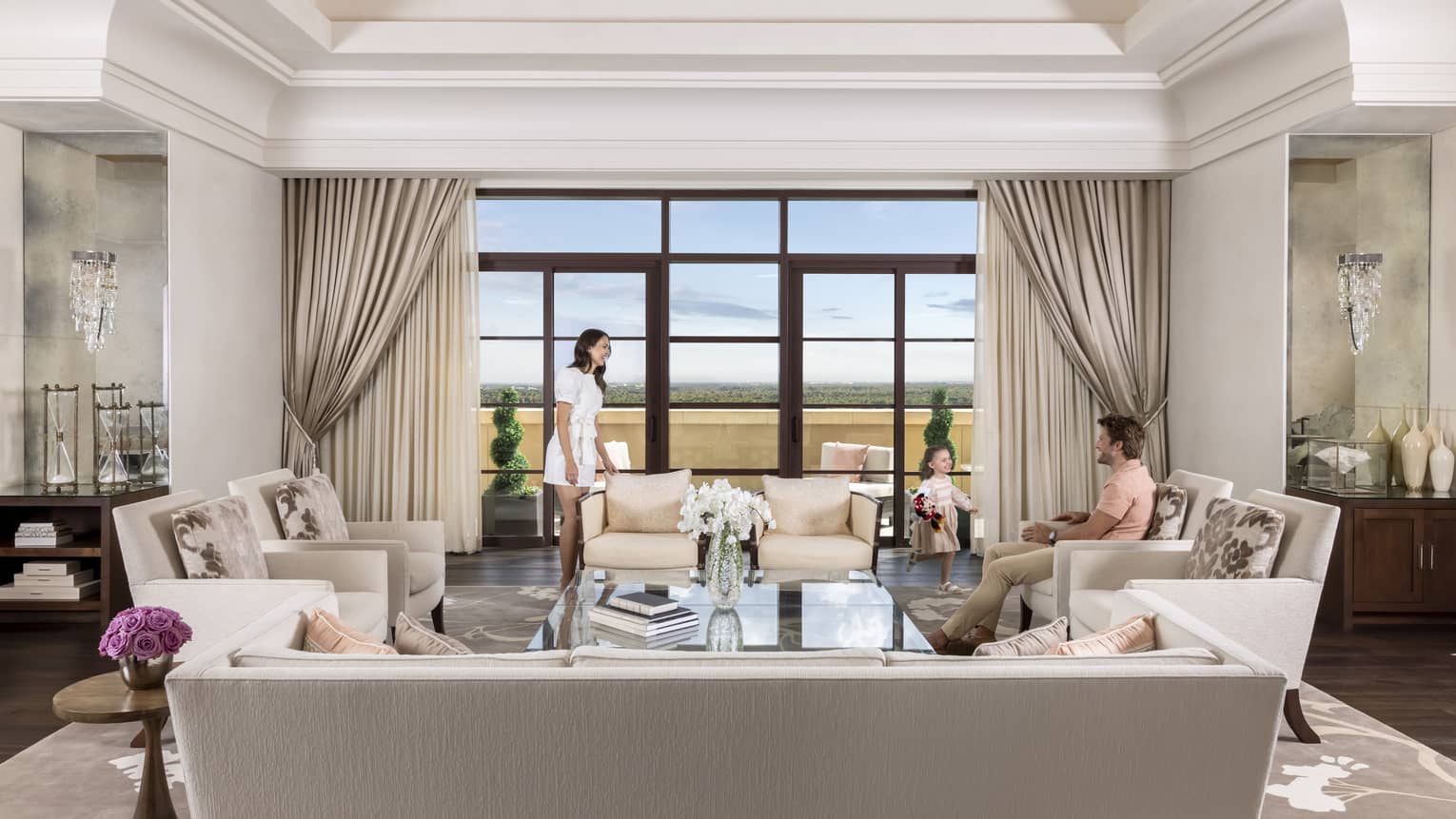Elegant living room with man, woman and young girl, facing wall of windows