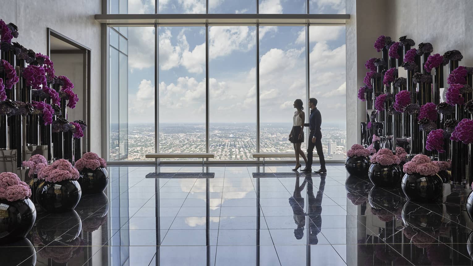 A man and woman walk in front of floor to ceiling windows in the pink flower lined lobby at Four Seasons Hotel Philadelphia
