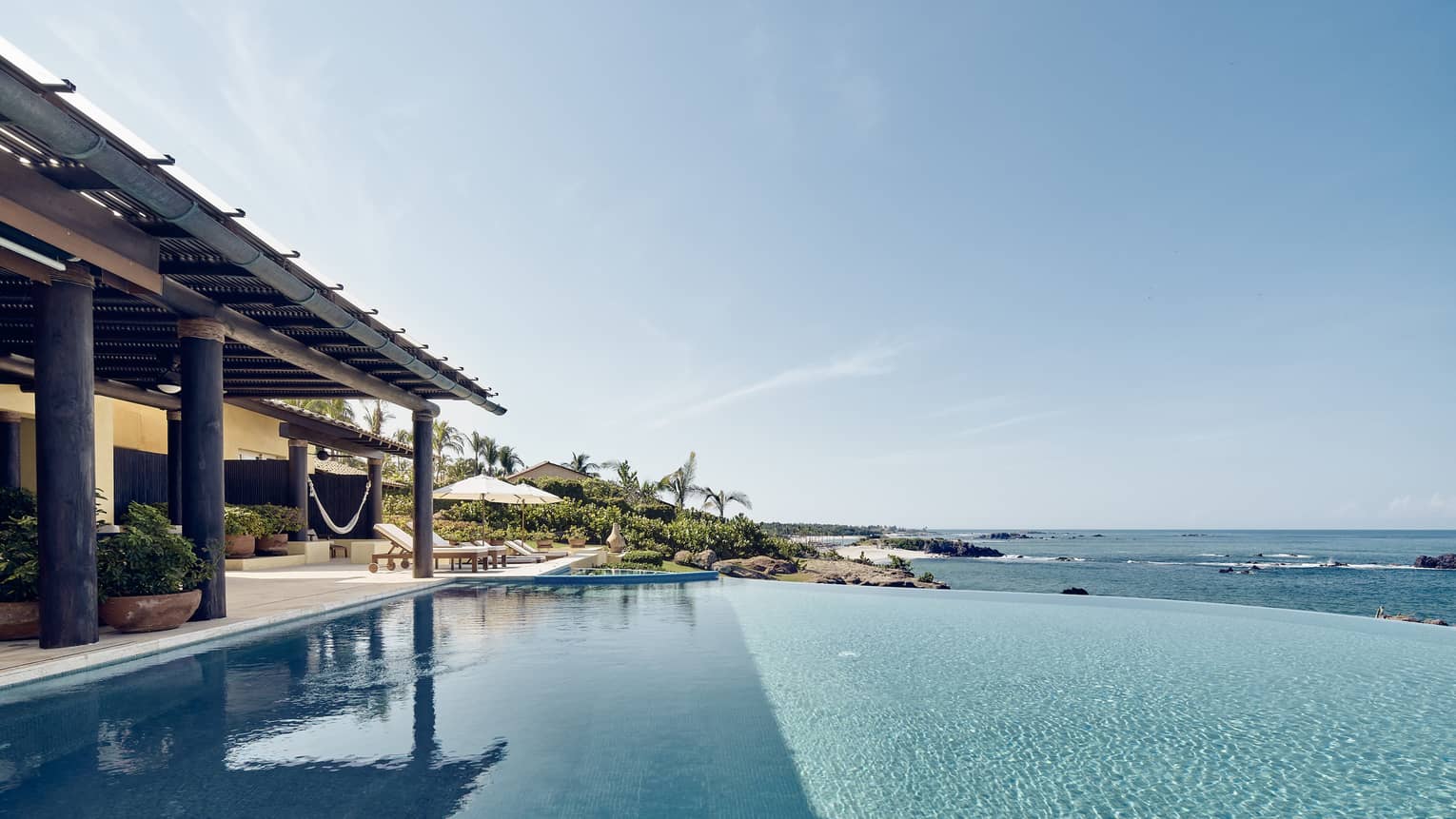 View over infinity swimming pool looking over ocean, covered patio at side