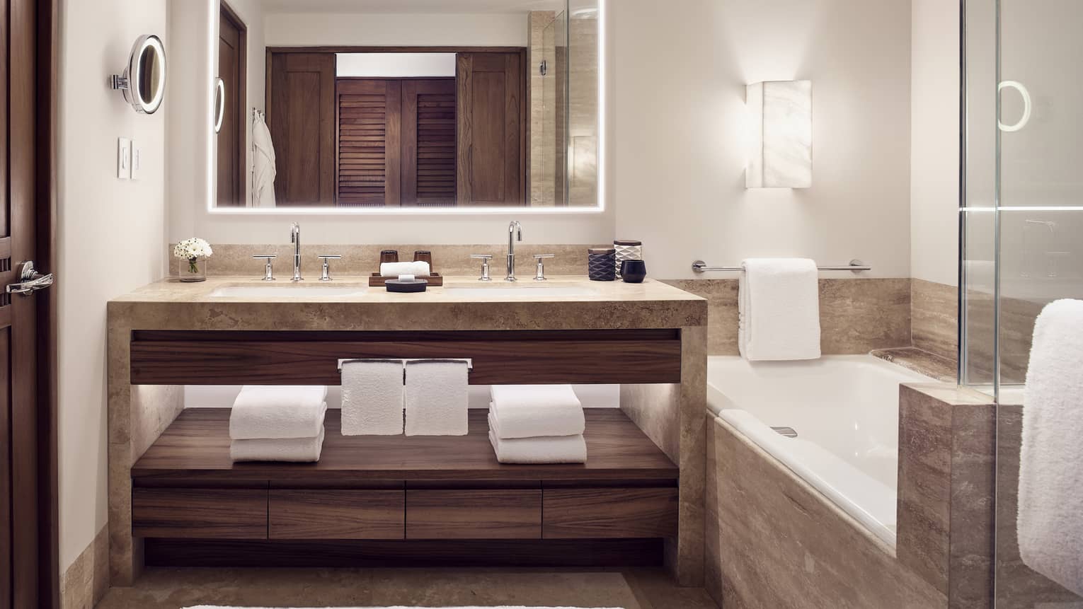 Bathroom with light stone double vanity, built-in tub, illuminated mirror