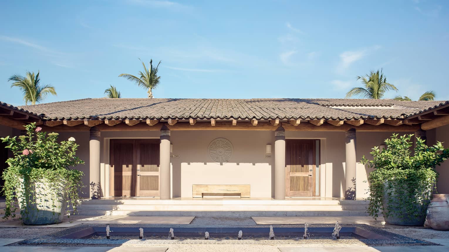 Arena Beach House exterior with shingled roof and stucco columns, large potted planted on either side of doorway