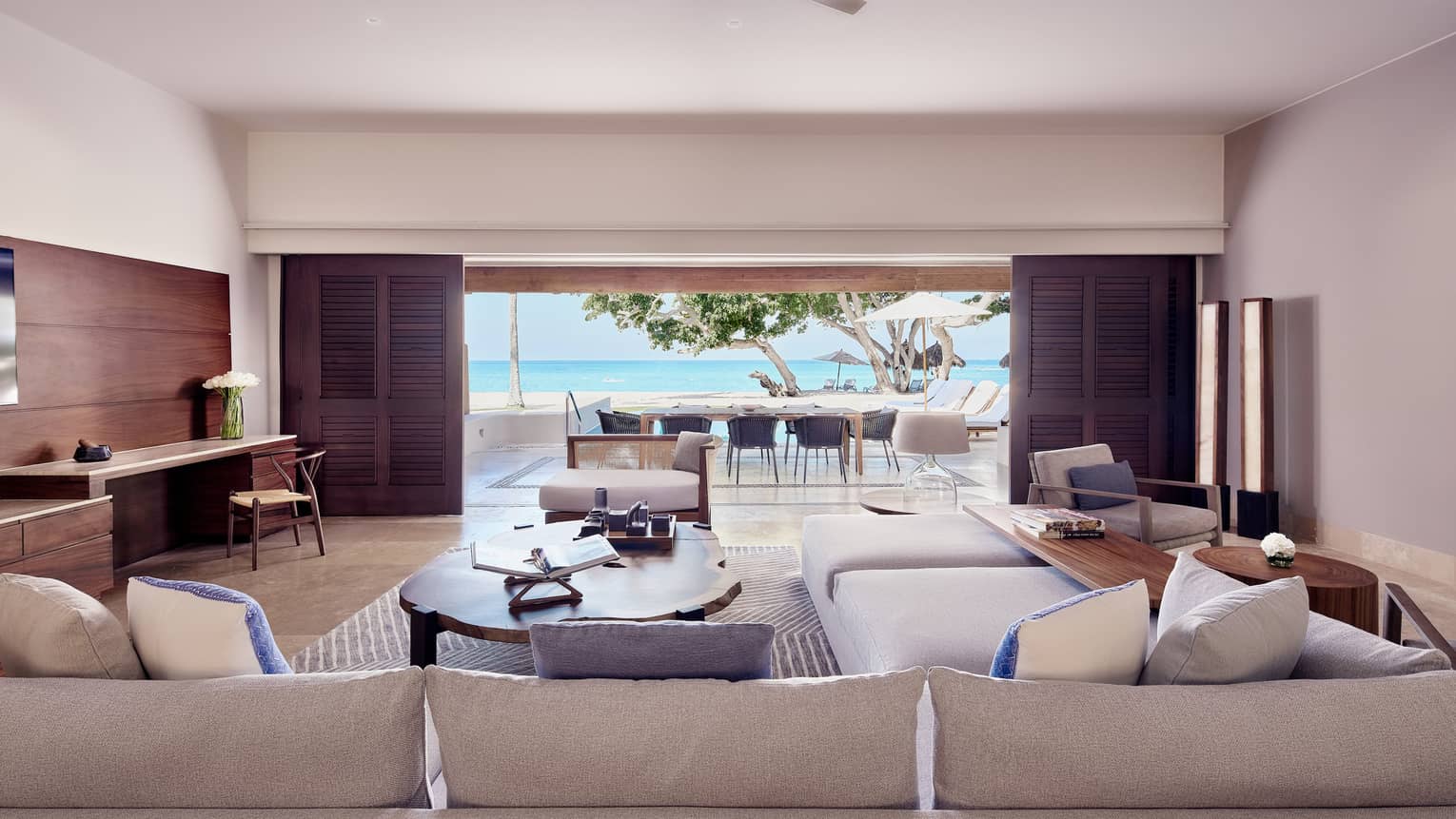 Arena Beach House living room with cream sectional sofa, large oak coffee table, doors open to outdoor dining area and pool