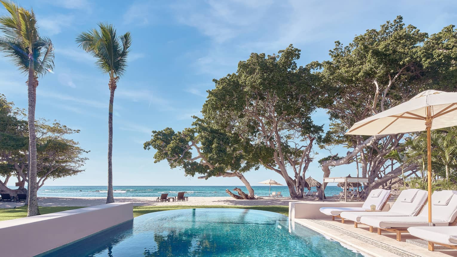 Arena Beach House pool with white lounge chairs, umbrella, palm trees, ocean views
