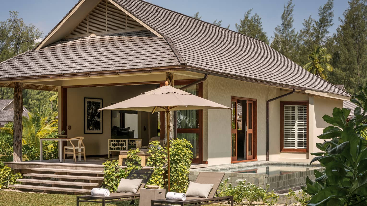 Exterior view of bungalow villa with two patio lounge chairs, umbrellas on lawn