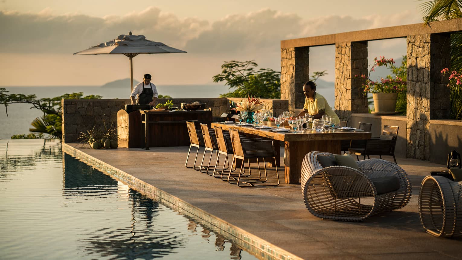 Six-Bedroom Residence Villa close-up of server setting long dining table by swimming pool at sunset 