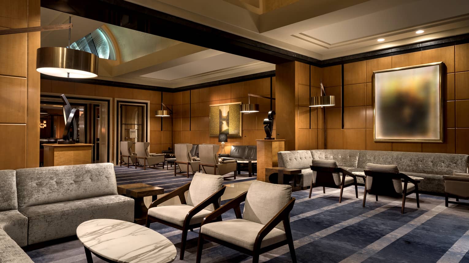 A lounge and lobby area with dark blue carpeting, grey chairs and sofa, and wood walls.