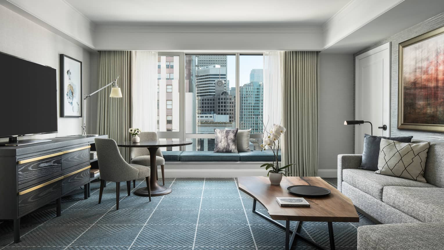 Living room with dark grid-like carpeting, sofa, wooden coffee table, TV, round table and chairs