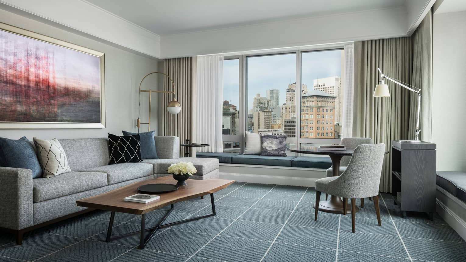 Hotel room with modern seating area, grey sofa by large window with padded bench