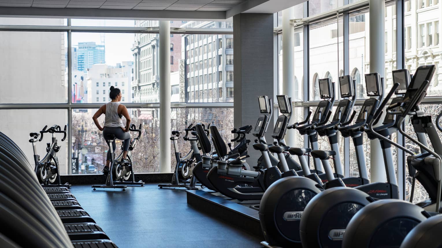 Equinox Fitness Centre, woman on exercise bike by floor-to-ceiling windows, row of cardio machines