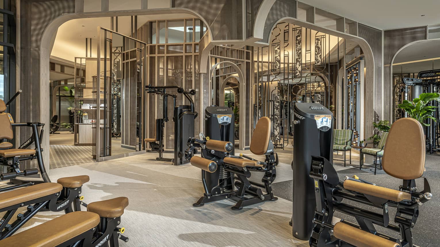 Fitness room with tan and black equipment, high ceilings, potted greenery