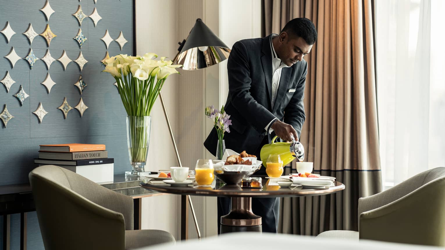 Hotel staff pours coffee from carafe into cup on brunch tray on in-room dining table