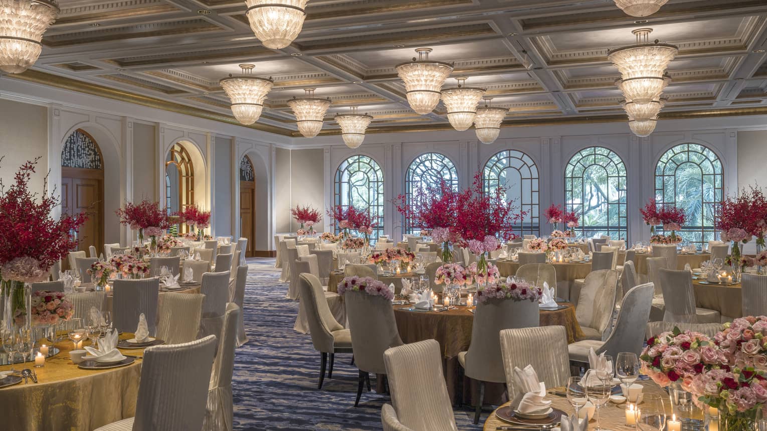 Circular tables are set for a meal and decorated with candles and pink and red bouquets
