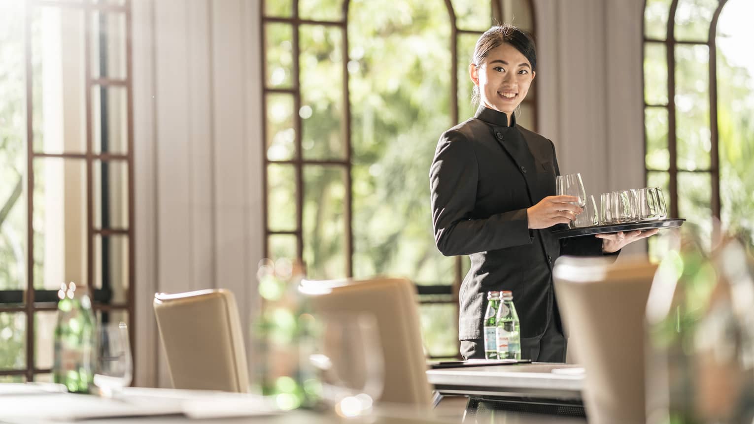 A female employee places glasses onto tables as she prepares the room for a meeting