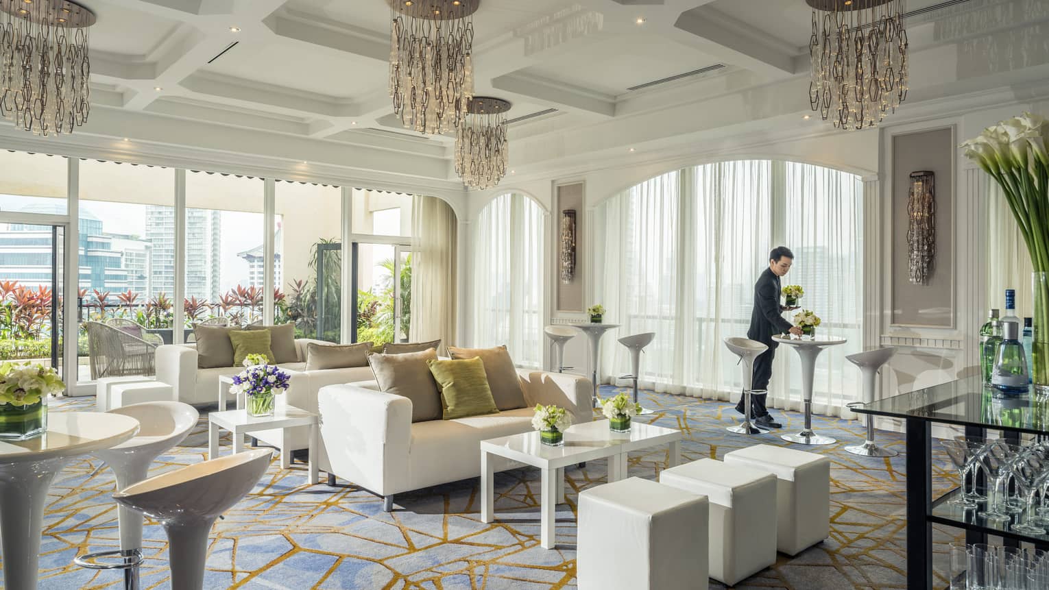 A bright room is decorated with plush couches, tables with flowers and artistic chandeliers