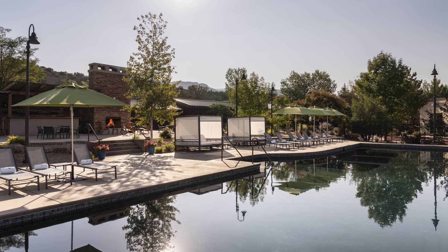An outdoor pool near trees, lounge chairs, and green umbrellas.