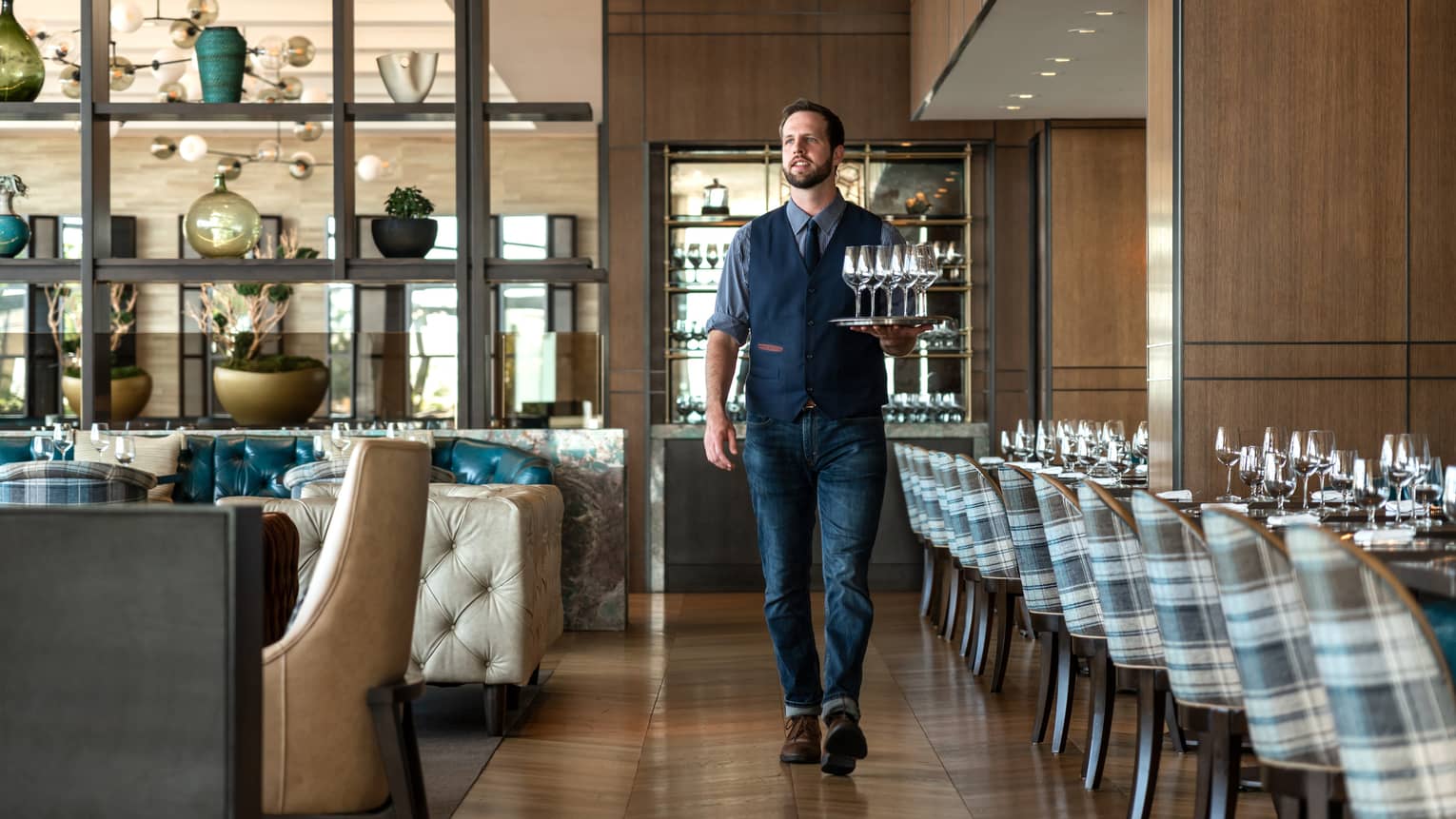 A team member carrying drinks on a tray in a well lit restaurant.