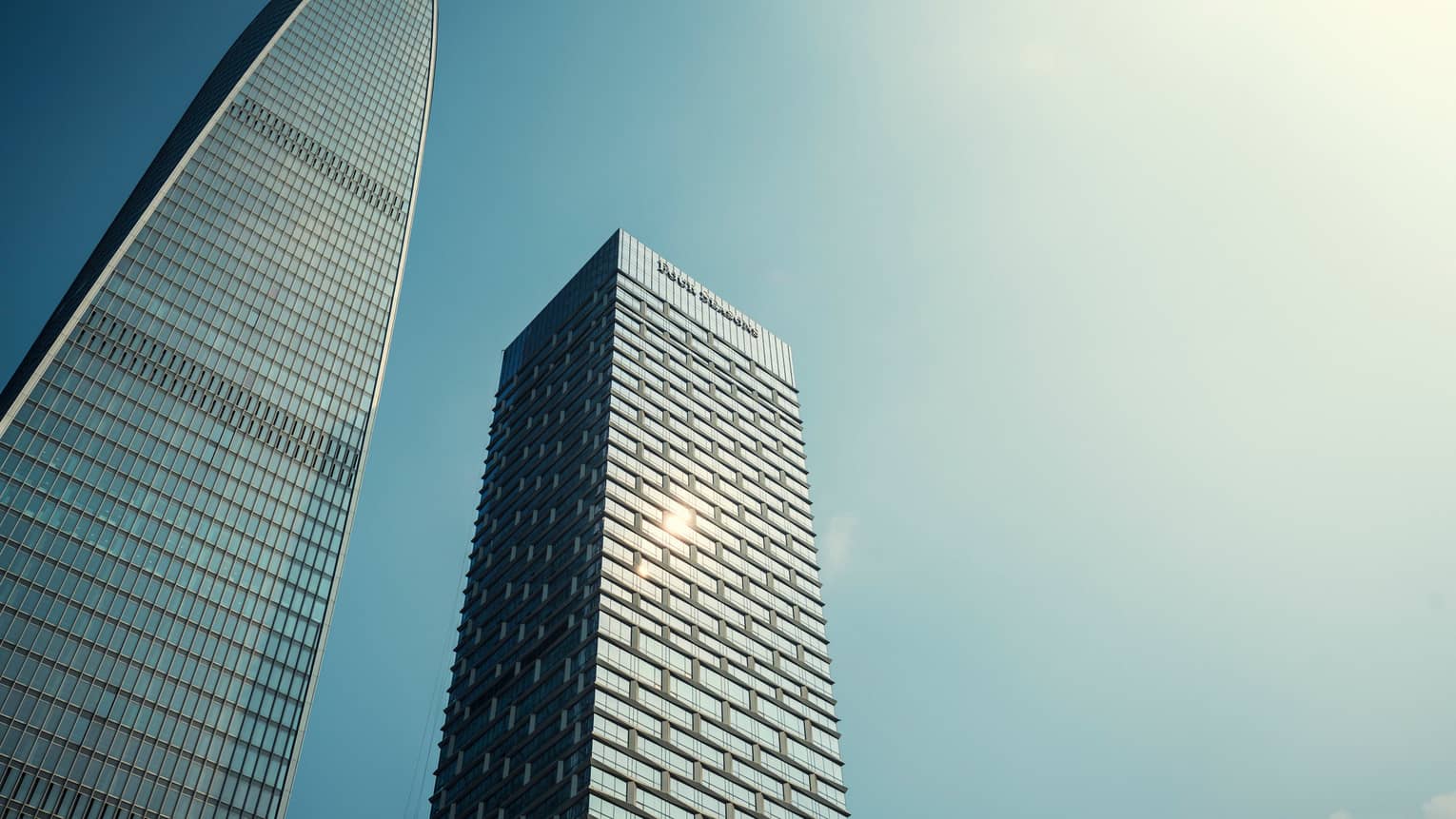 Looking up at two soaring glass towers against blue sky 