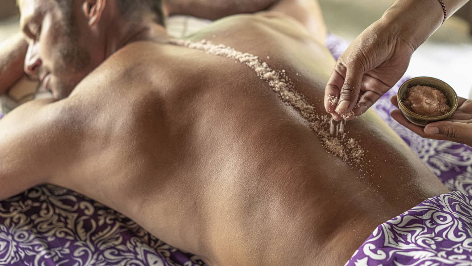 Hand place spa salts along man's spice during Sacred River Spa Massage