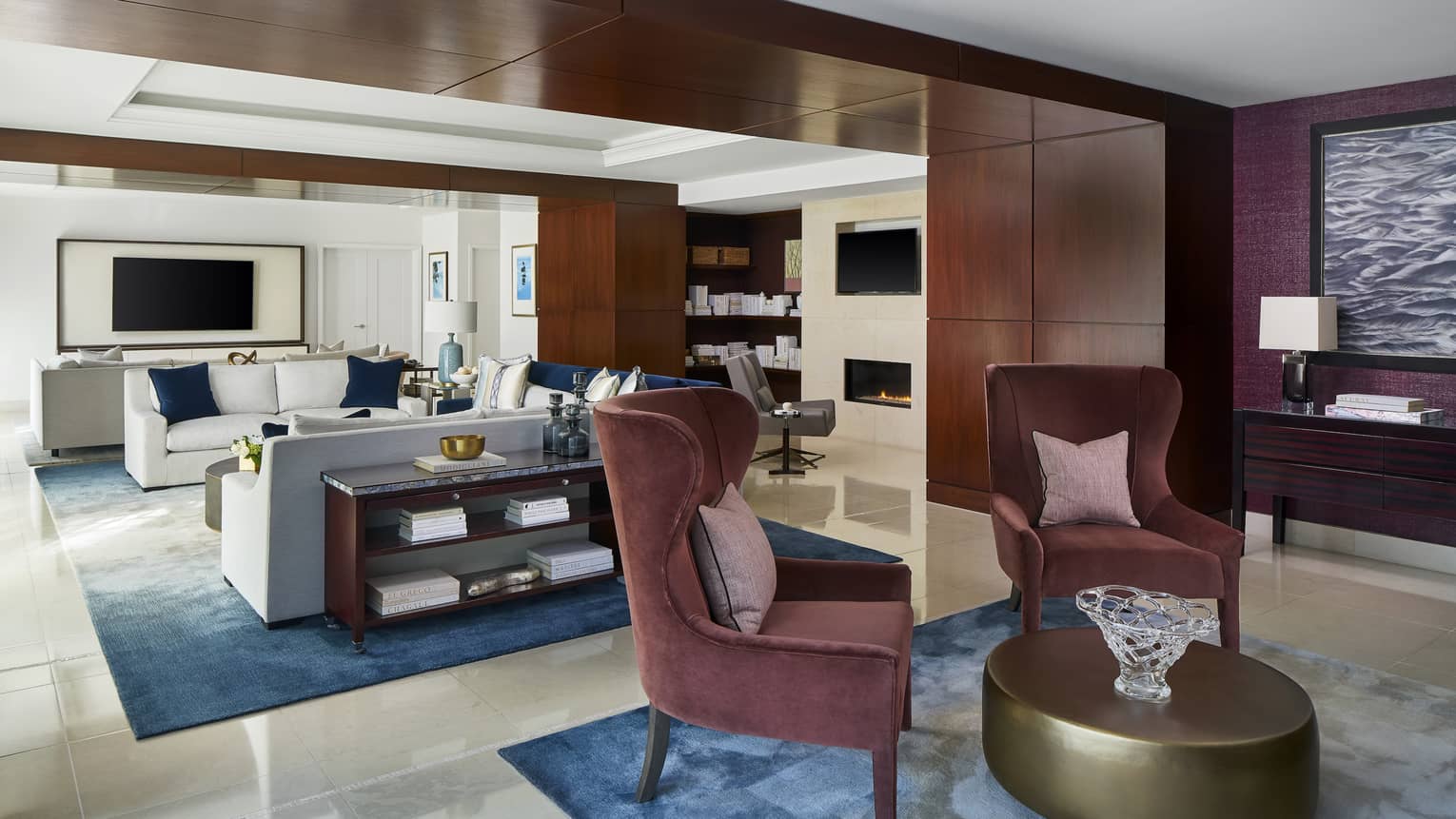 Sitting room with two maroon upholstered chairs, gold circular coffee table, connecting to light-filled living room