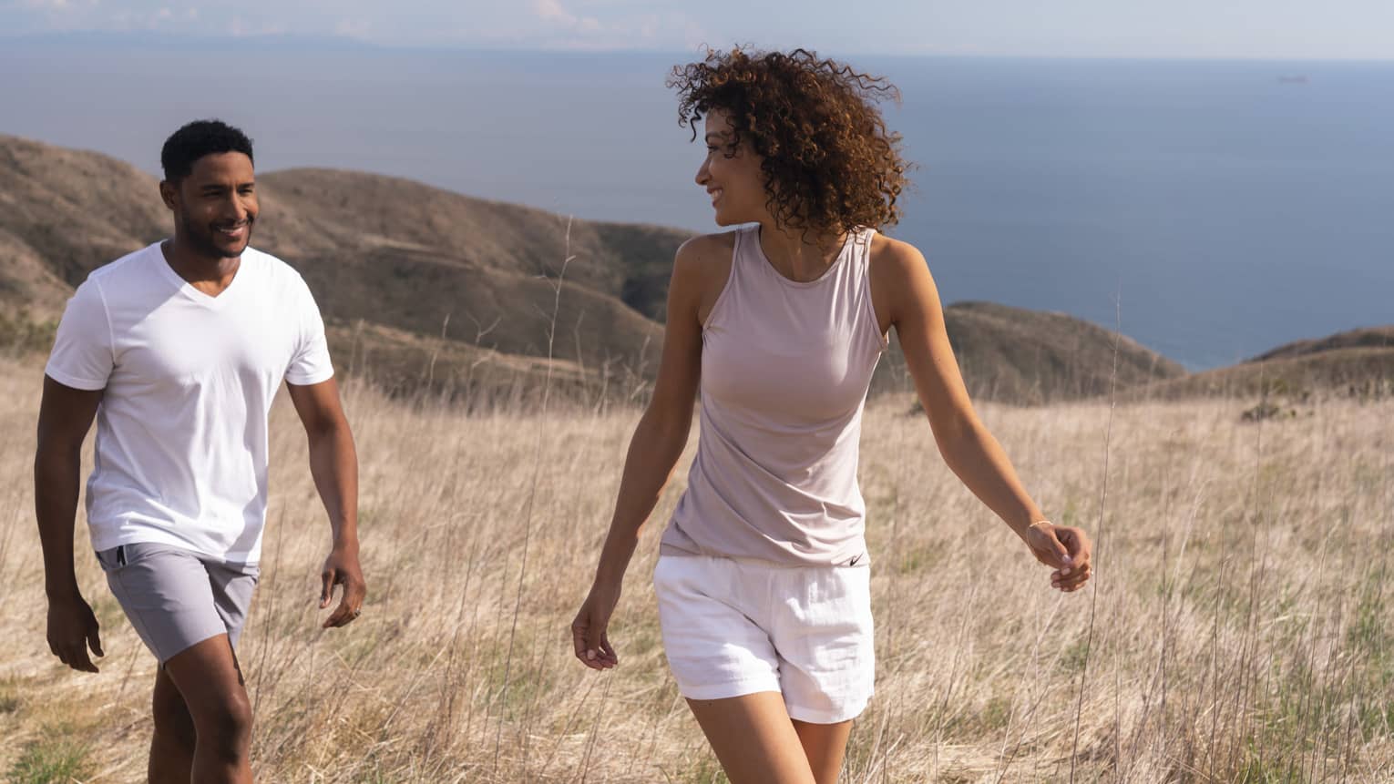 A woman and man walking through a large field and smiling at each other.