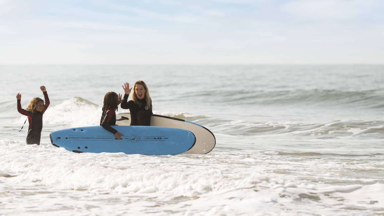 A mother and two children walking with surfboards through water.
