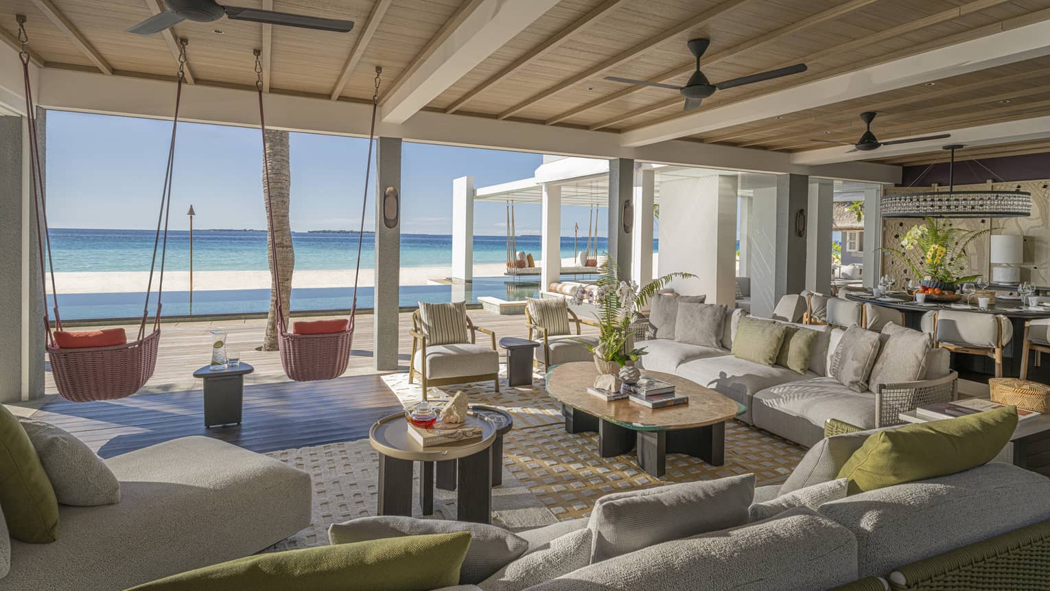 Large living room of private estate opening to a beachfront pool terrace with two hanging chairs