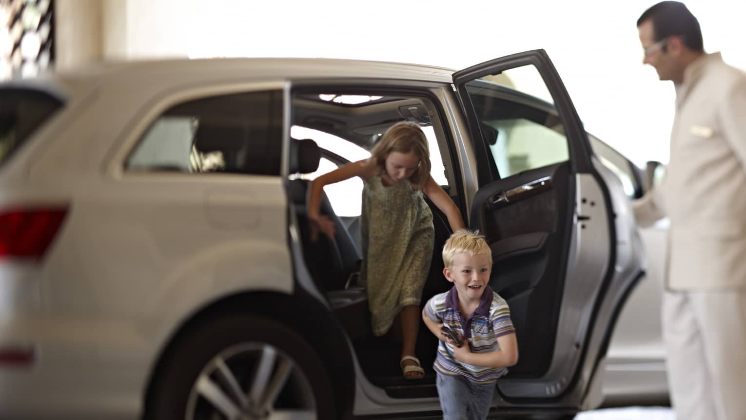 Man opens parked car door as two smiling children jump out