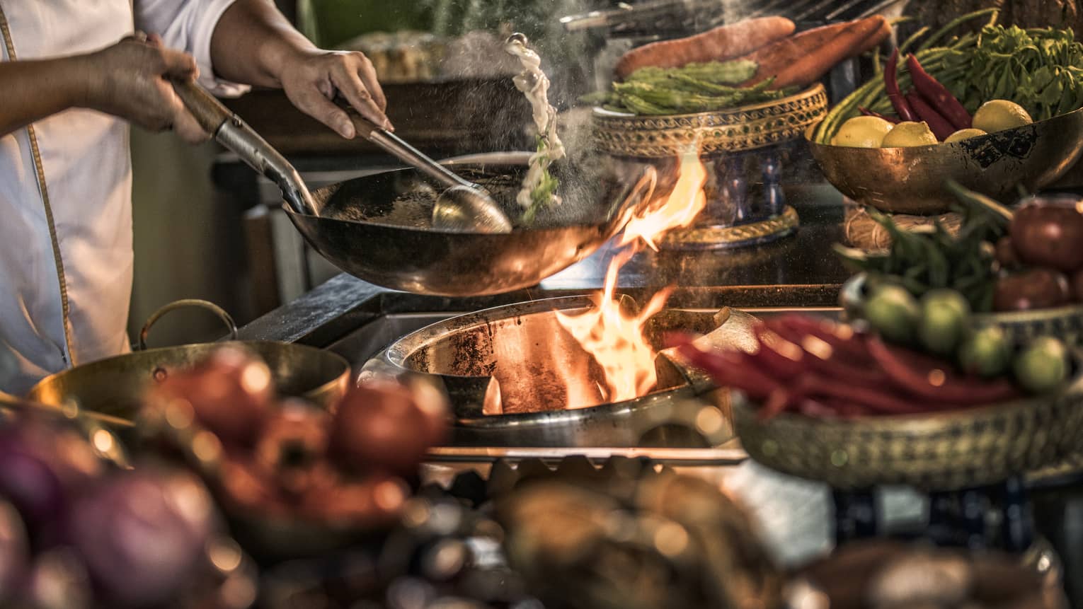 Close-up of chef stirring meals in copper pans over stove, flames