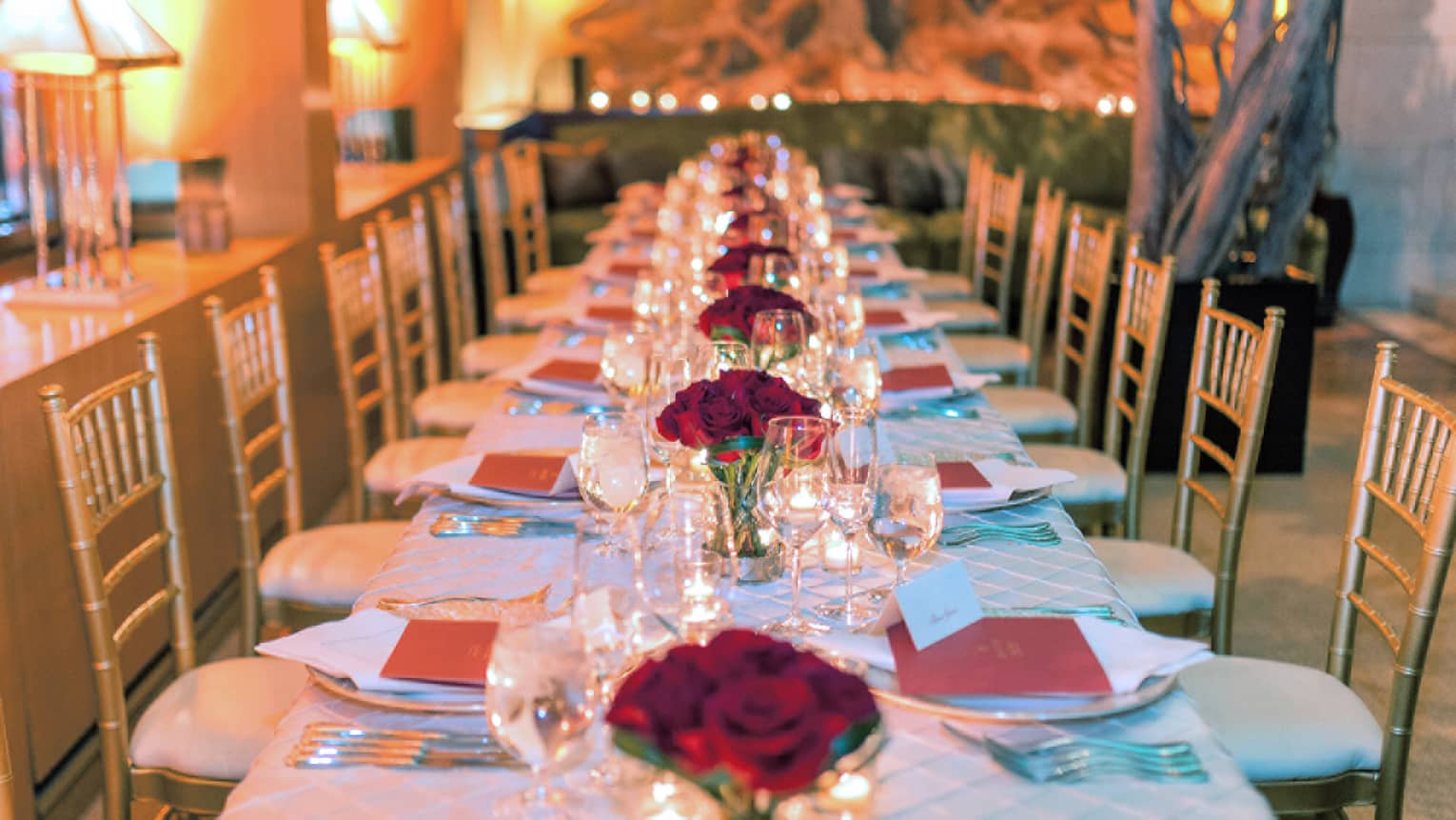 Long banquet dining table with red roses in vases down centre