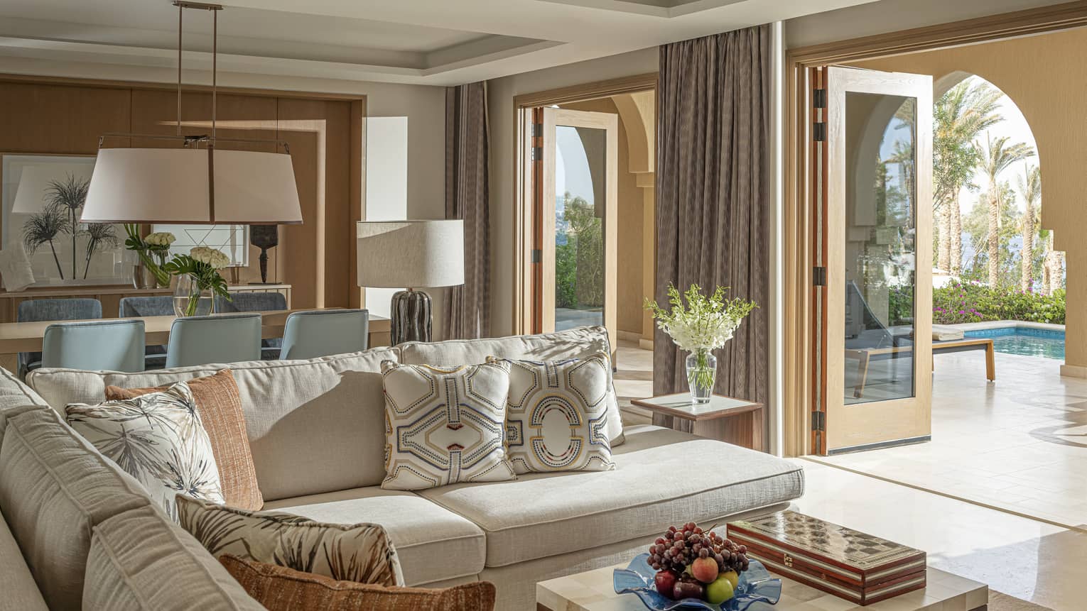 Imperial Suite living and area with cream sectional, marbled coffee table, rectangular dining table with blue chair, doorway to terrace