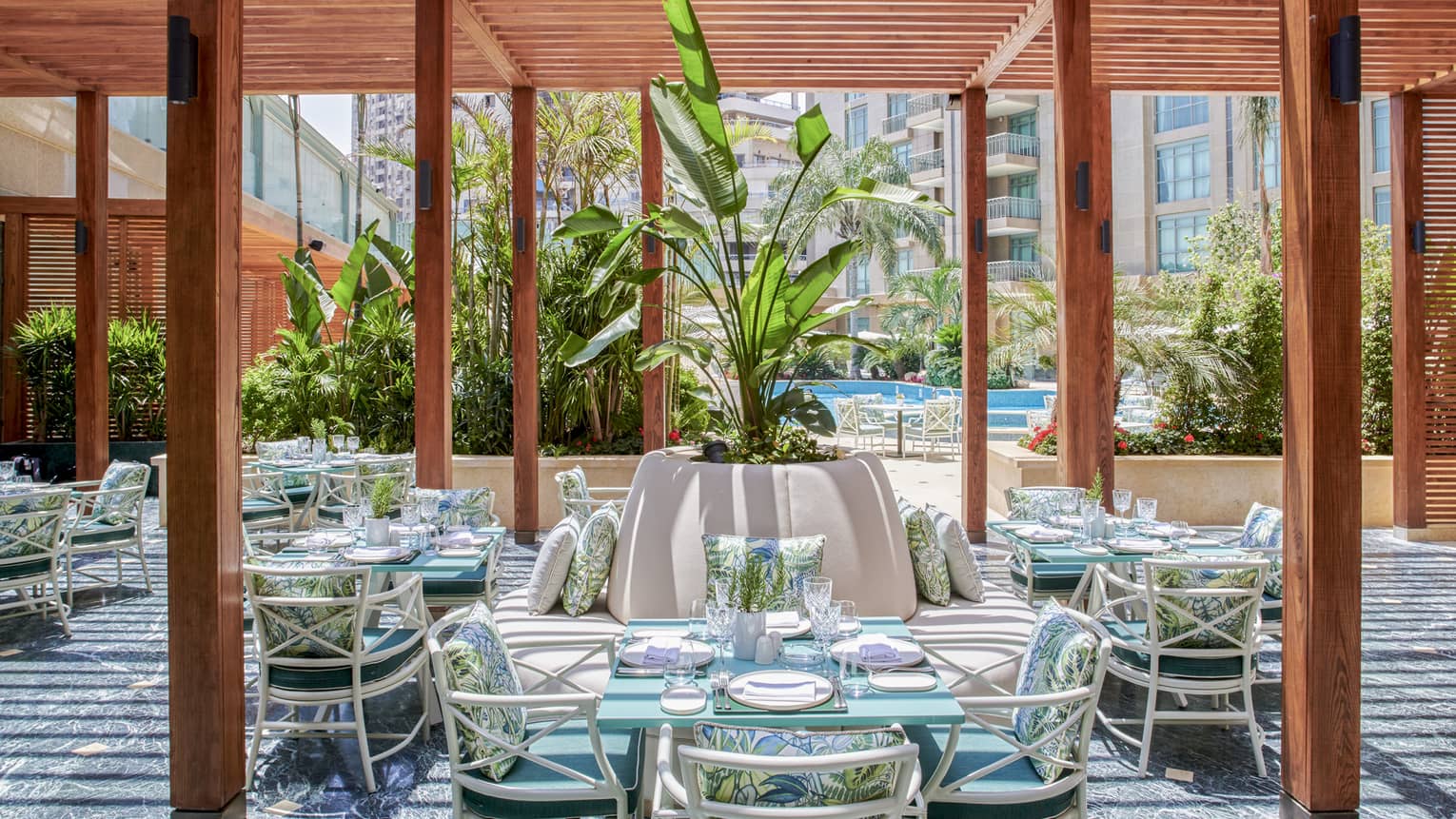 Byblos restaurant outdoor dining space with wooden columns, rattan chairs and square tables, large potted plant in middle