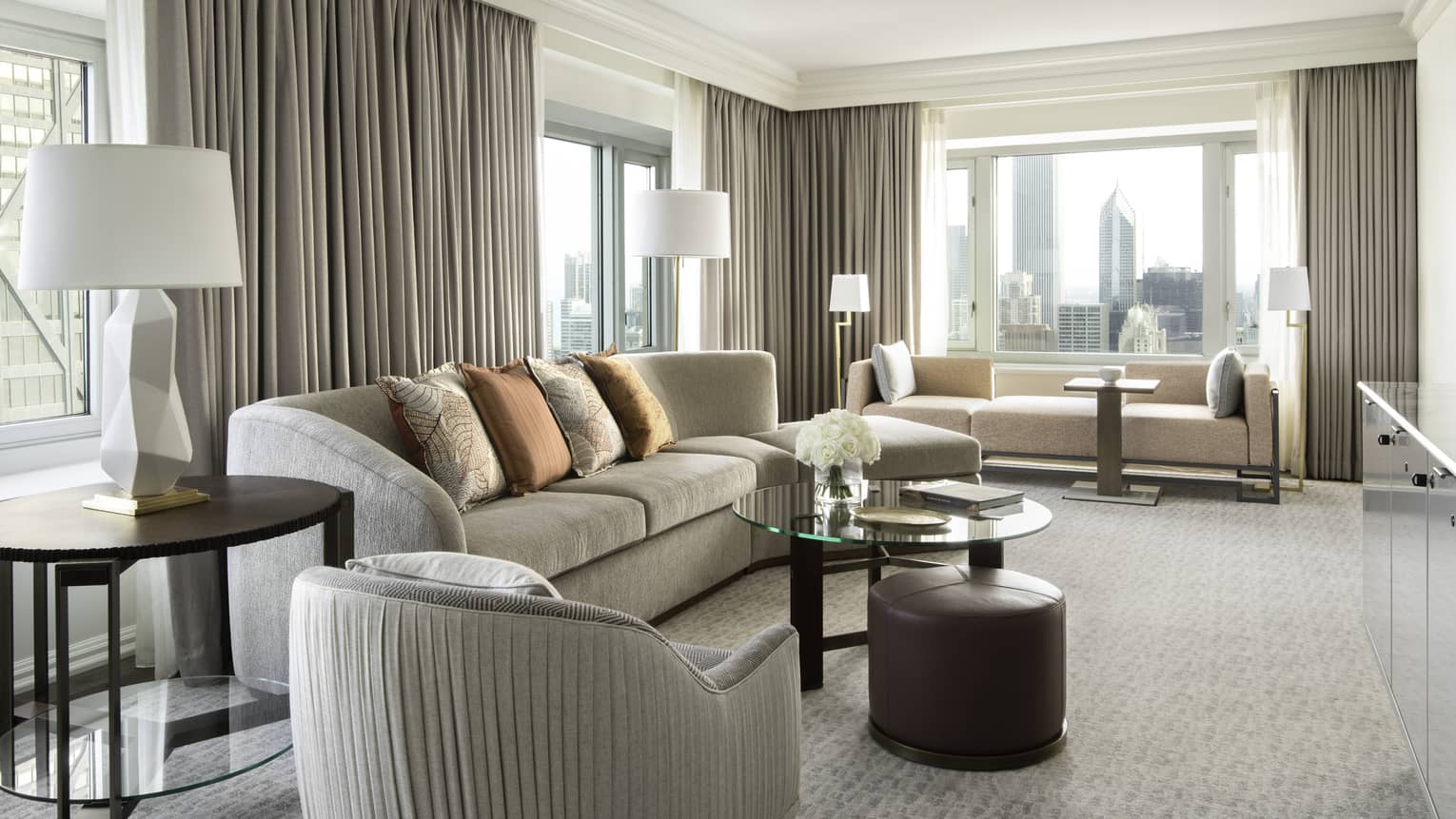 Living area with grey sofa, glass table, beige carpet, grey curtains, large windows