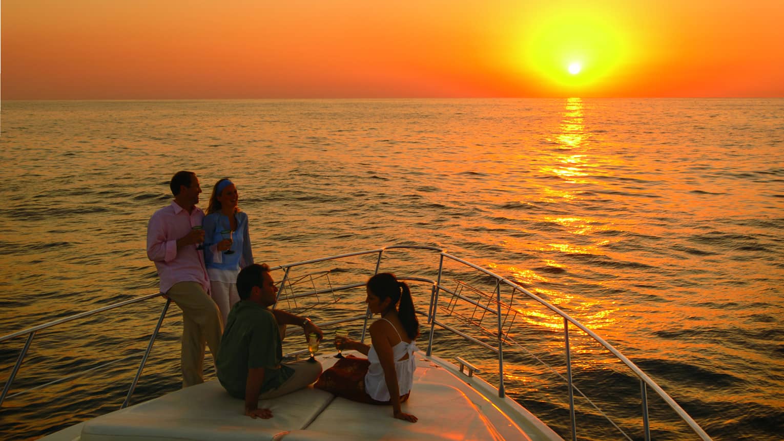 Two couples drink wine on Four Seasons boat at sunset 