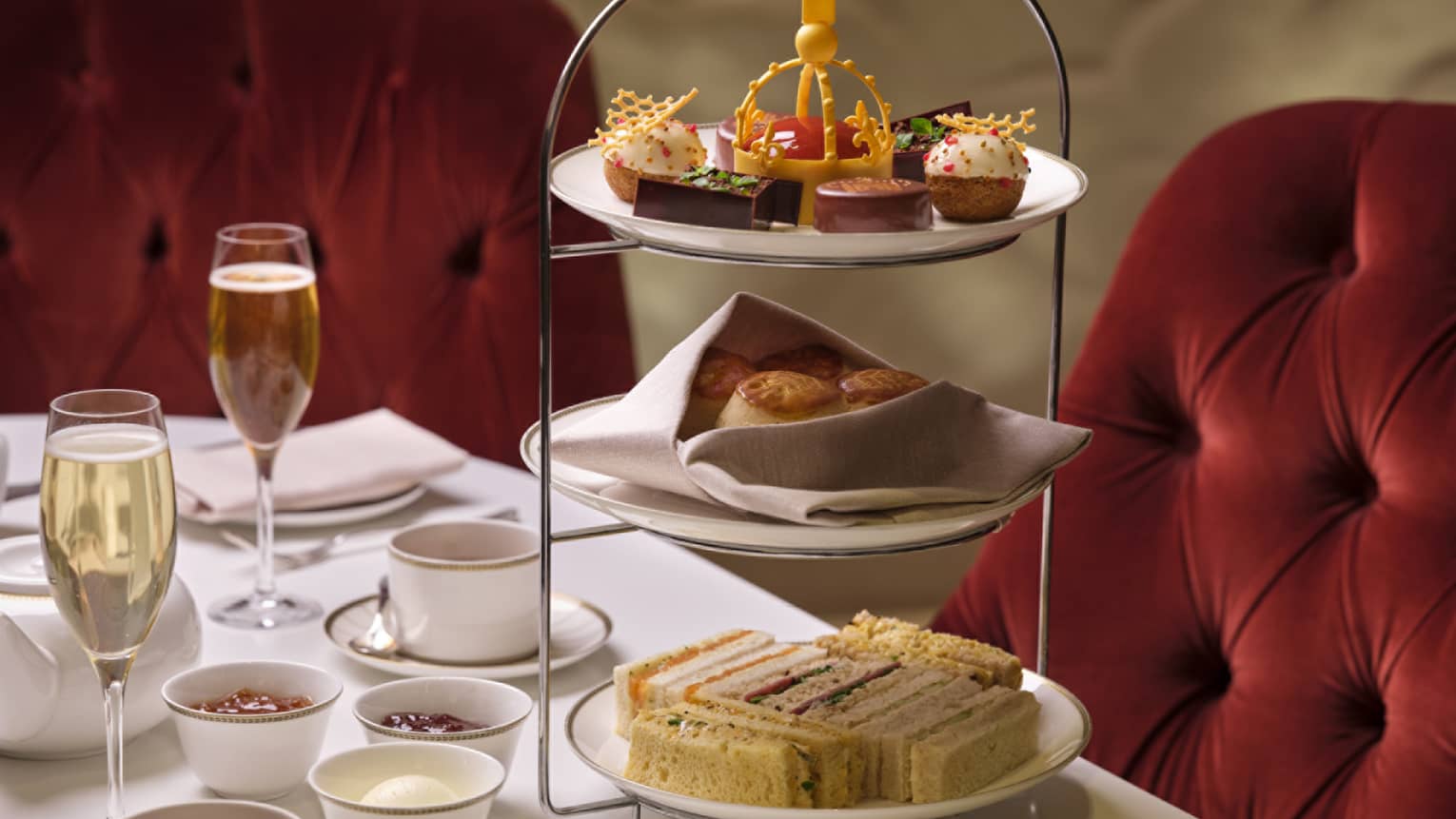 Tea stand with finger sandwiches, treats and small bites on table beside tea and champagne