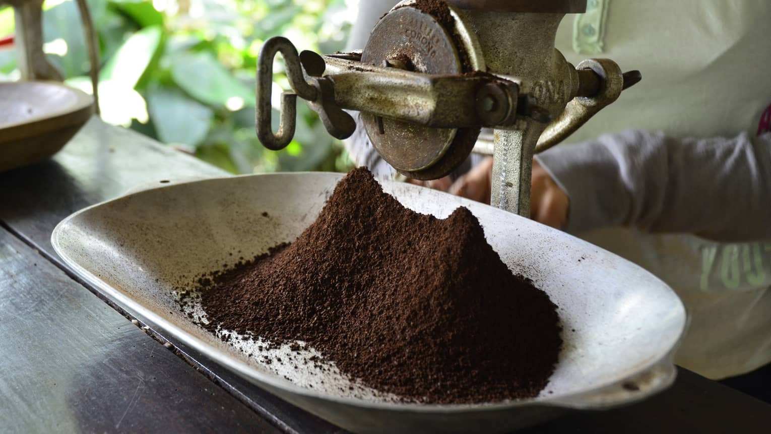 Large metal industrial-looking hand grinder with pile of ground Colombian coffee 