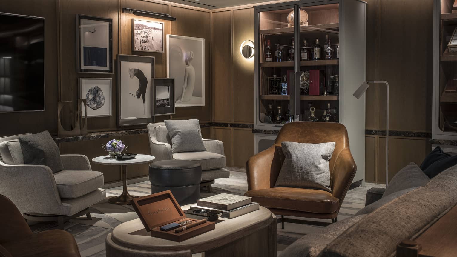 A dimly lit cigar lounge, showing three arm chairs and different sized framed artwork on wall