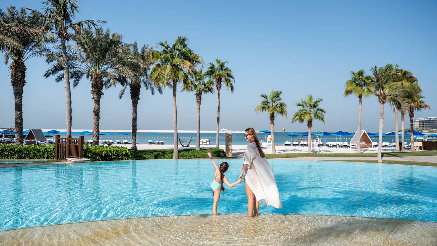 A woman and a little girl hold hands while wading in the outdoor pool overlooking the Arabian Gulf