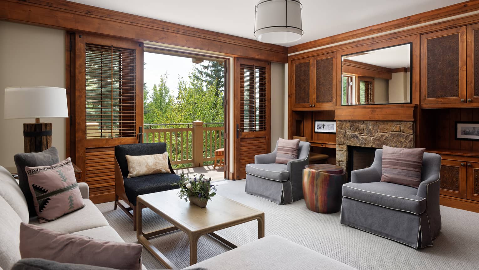 Mountain-chic living room with sofa, grey arm chairs, stone fireplace, mirror and walk-out balcony