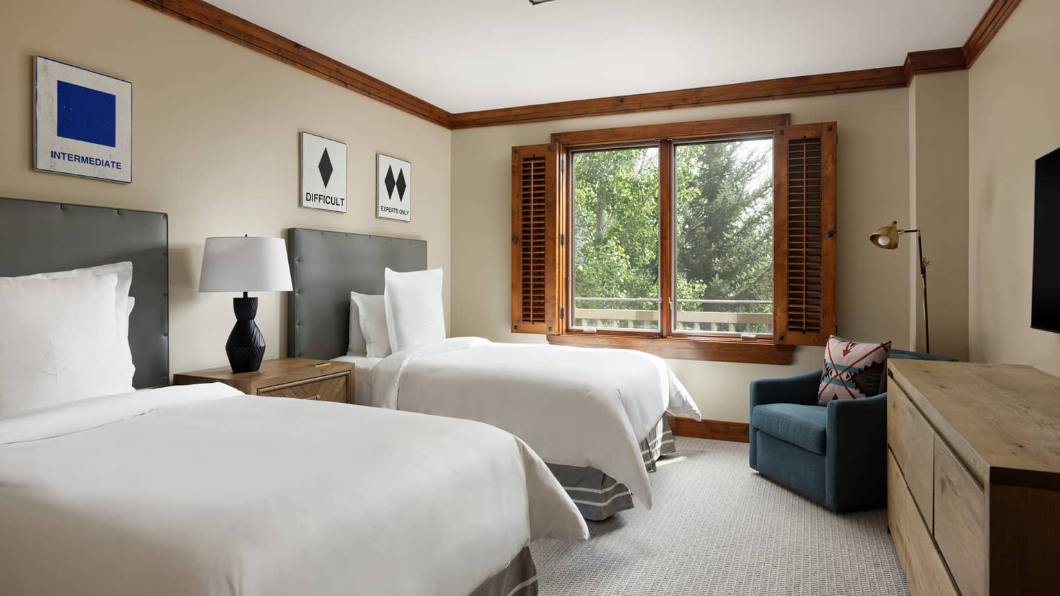 Bedroom with two twin beds, dresser, arm chair and window with wooden shutters