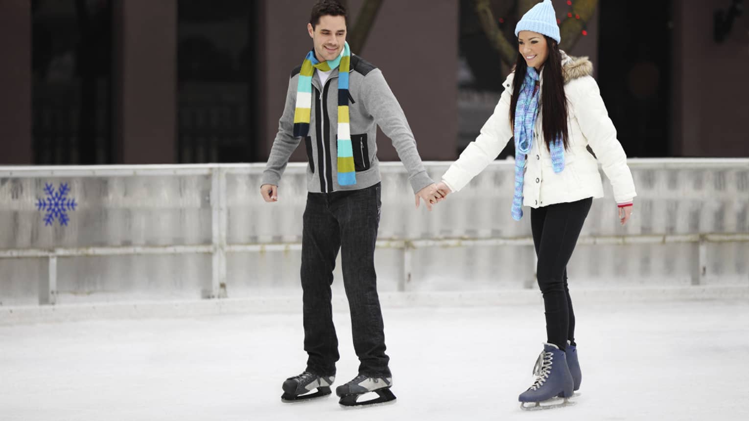 Couple wearing winter coats, hats and scarves ice skating 