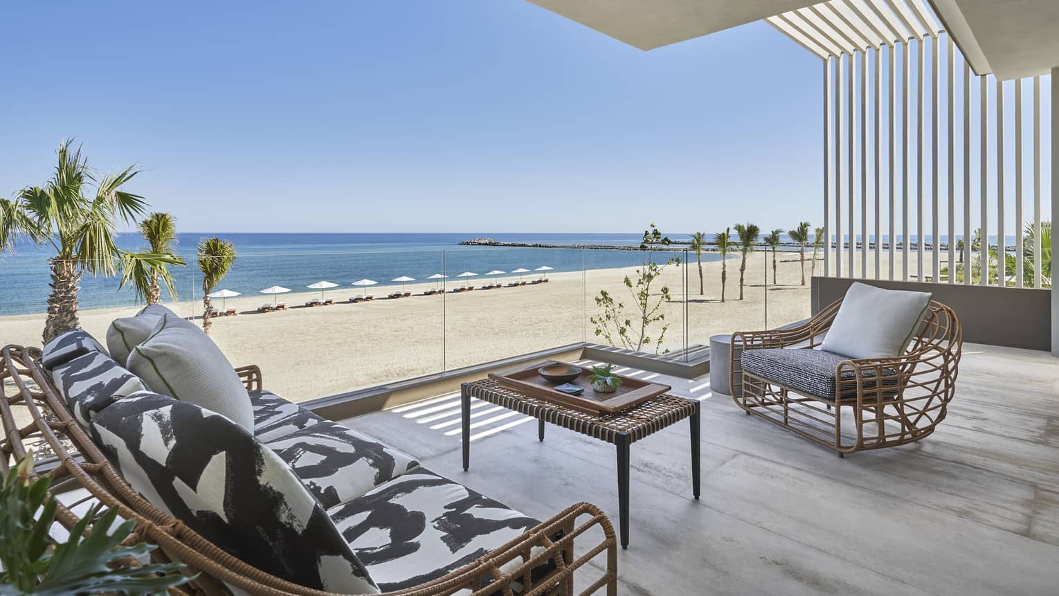 Outdoor terrace with modern wicker sofa and arm chair, glass railing, beach and ocean view